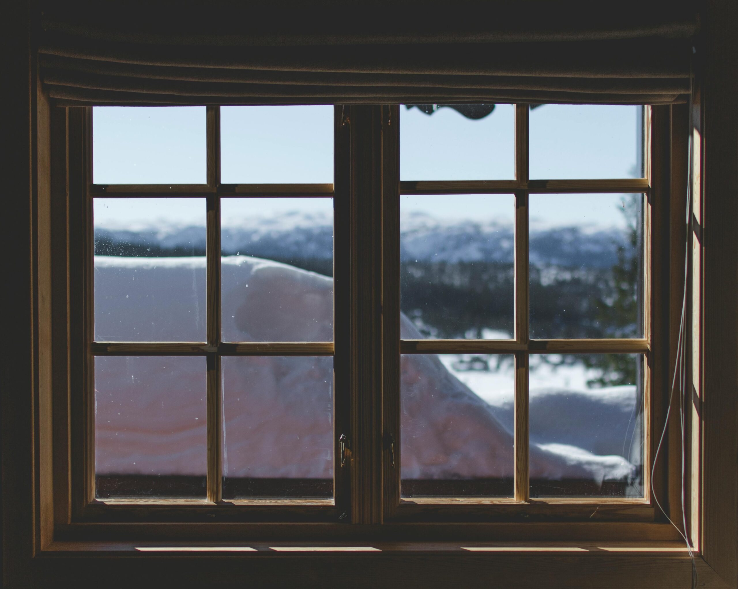 A scenic view of snow-capped mountains through a wooden window frame, capturing the serene winter landscape.