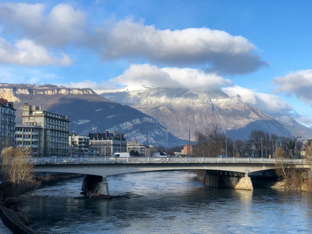 pexels-photo-5388514-5388514 Explore the stunning landscape of Grenoble with mountains, river, and architecture under a blue sky.